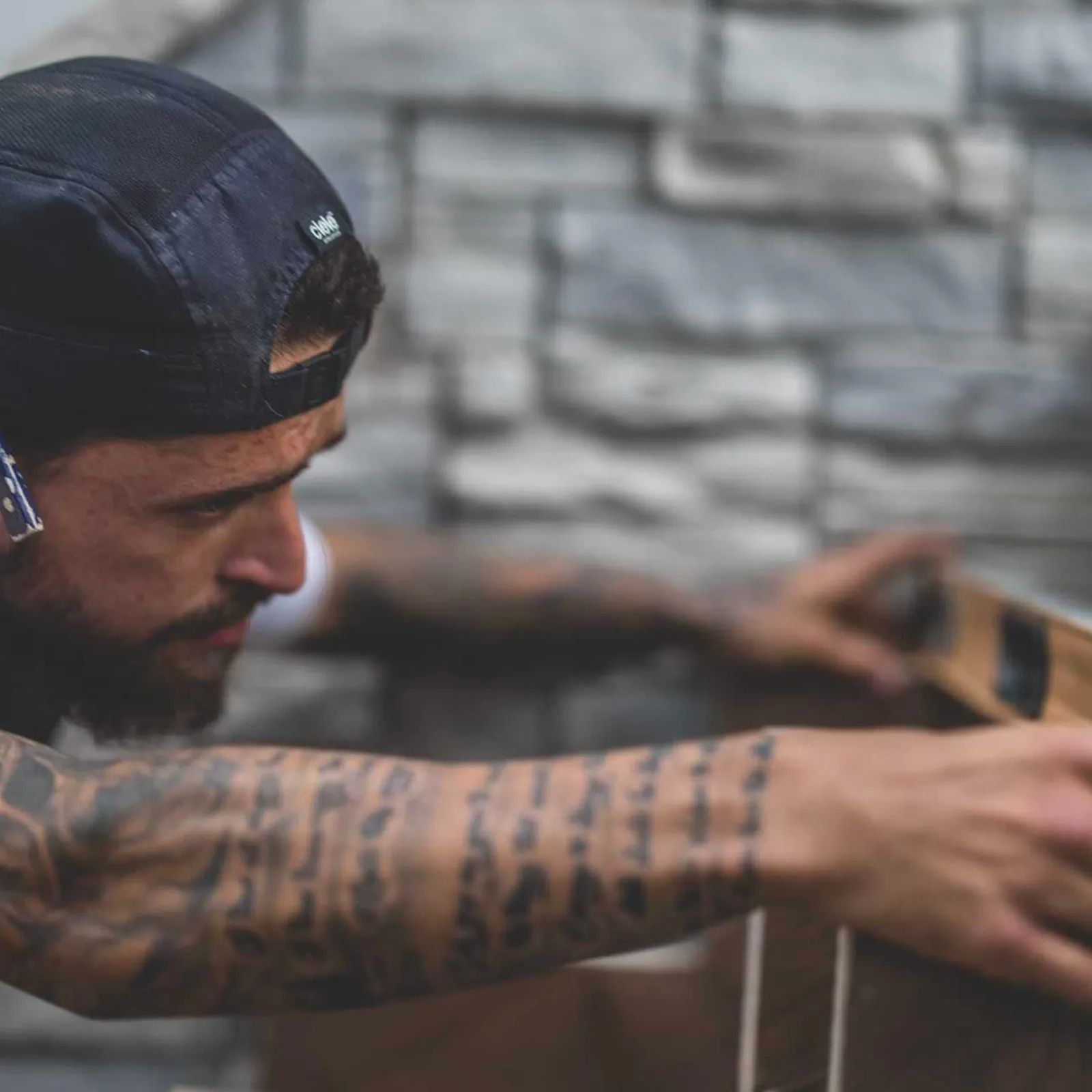 Travailleur de la construction, casquette à l'envers et avant-bras tatoué, ajustant un niveau contre un mur de pierre sur un chantier de rénovation